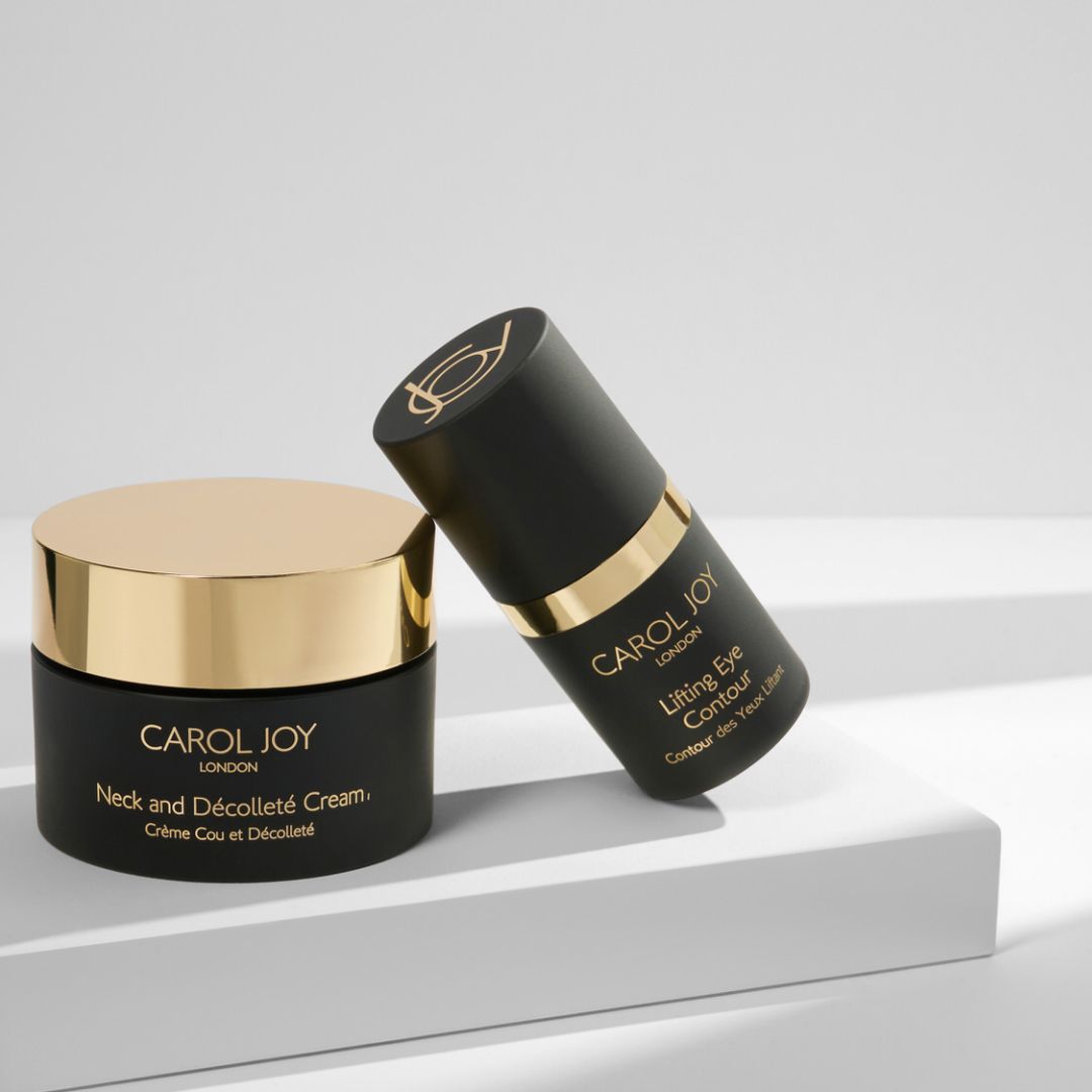 The Carol Joy London Neck And Décolleté Cream on a display stand with the Carol Joy London Lifting Eye Contour leaning against its right side, against a plain white background