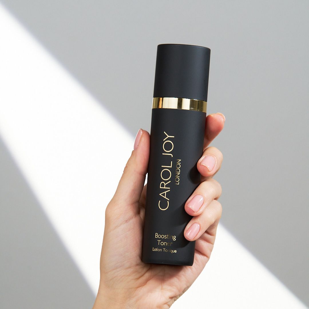 Hand holding the Carol Joy London Boosting Toner against a white wall