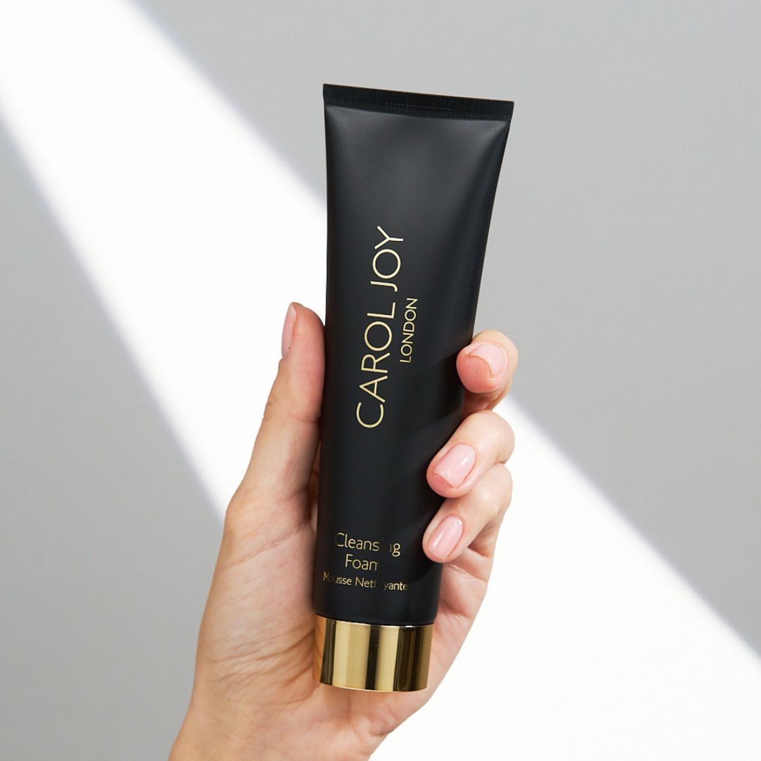 Hand holding the Carol Joy London Cleansing Foam against a plain white wall
