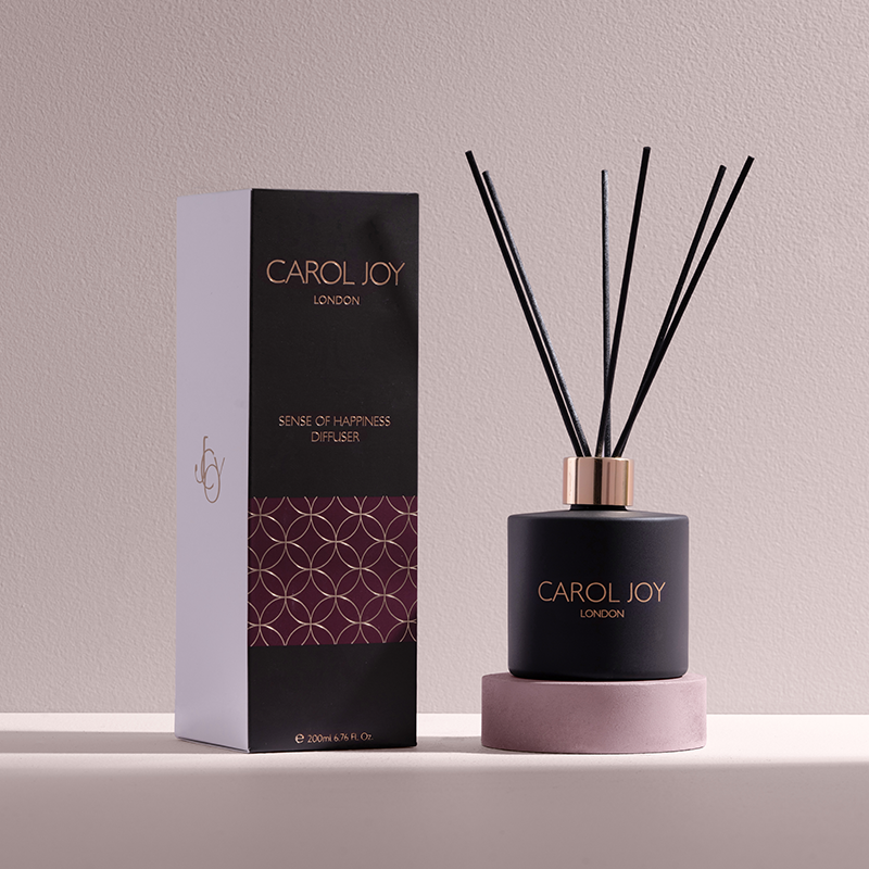 The Carol Joy London Sense Of Happiness Diffuser against a plain background, its packaging to the left